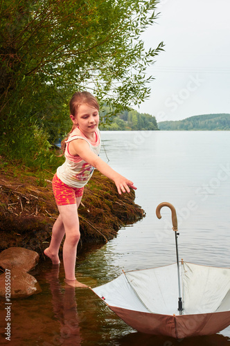 Little girl lost her umbrella in cloudy day in the lake