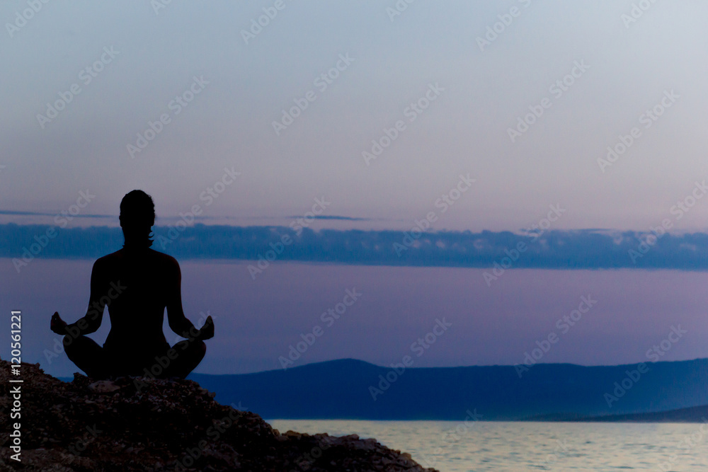 Silhouette of Woman Meditating in Lotus Position by the Sea at Sunset. Rear View. Meditation Concept.