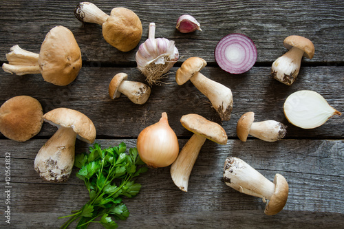 Fresh white mushrooms from forest with parsley and garlic on a rustic wooden board, overhead view.