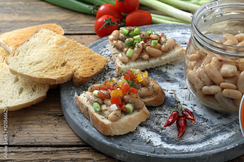 crostini di pane e fagioli bianchi con pomodoro su sfondo tavolo di cucina rustico