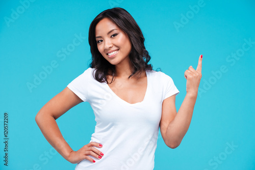 Cheerful young vietnamese girl pointing finger up at copyspace