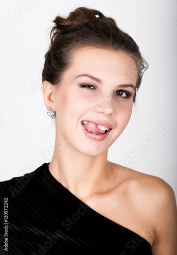 close-up fashion photo of young lady in elegant black dress, playful woman shows tongue