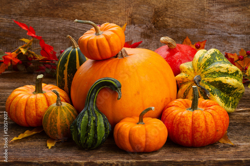 pile of orange and green pumpkins with fall leaves on wooden table