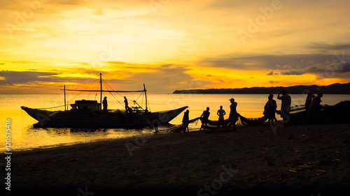 Fishermen dragging fishing net from boat to beach - Sunset silhouette in Aklan, Panay - Philippines