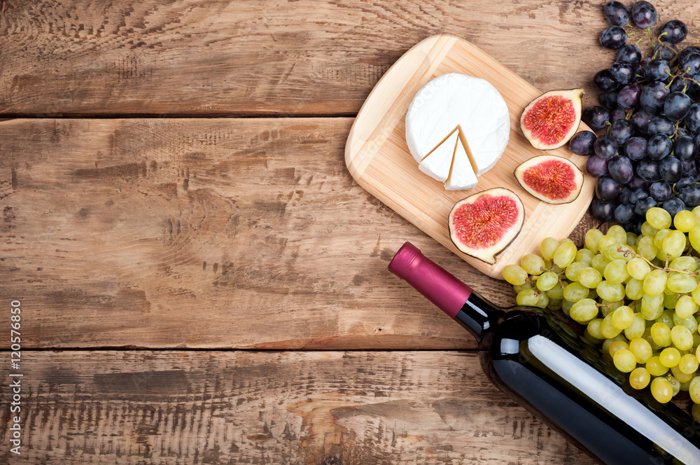 Bottle of red wine, grapes, cheese camambert and figs on old rustic wooden table. Food background. Top view Bottle of red wine, grapes, cheese camambert and figs on old rustic wooden table. Food background. Top view