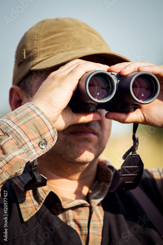 Man hunter with shotgun looking through binoculars in forest