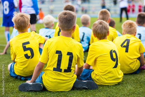 Children soccer football team at the sport stadium. Boys sitting on football pitch during school soccer tournament