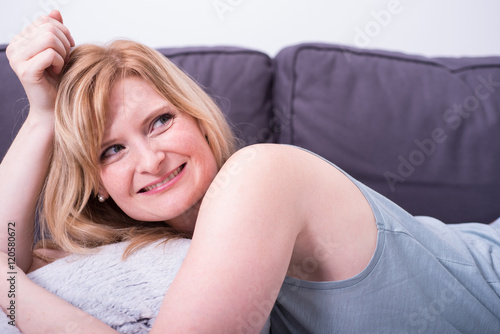 beautiful blonde woman is smiling and relaxing on gray couch