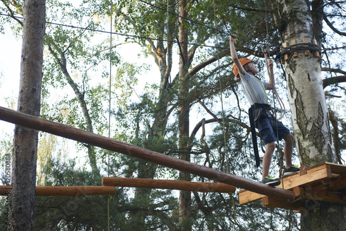 Portrait of active brave boy enjoying outbound climbing at adventure park on tree top