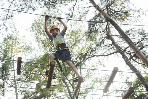 Portrait of active brave boy enjoying outbound climbing at adventure park on tree top © Petr Bonek