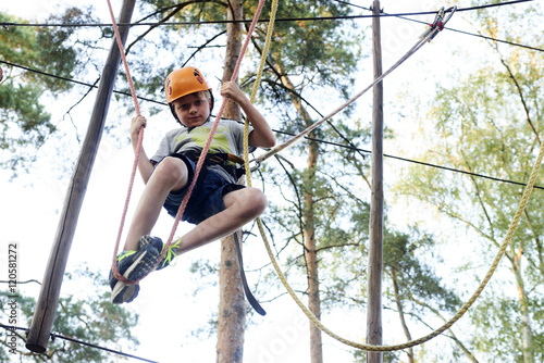 Portrait of active brave boy enjoying outbound climbing at adventure park on tree top