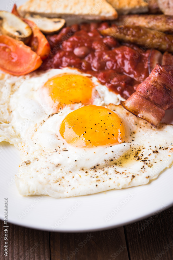 English breakfast (fried eggs, beans, roasted bacon, sausages and vegetables) close up. English breakfast (fried eggs, beans, roasted bacon, sausages and vegetables) close up.