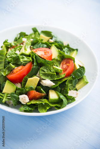 Fresh healthy salad with chicken, tomatoes, spinach and avocado on blue wooden background close up. Health and food.