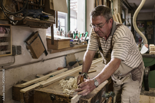 Craftsman in carpentry workshop smoothing wooden workpiece with planer photo