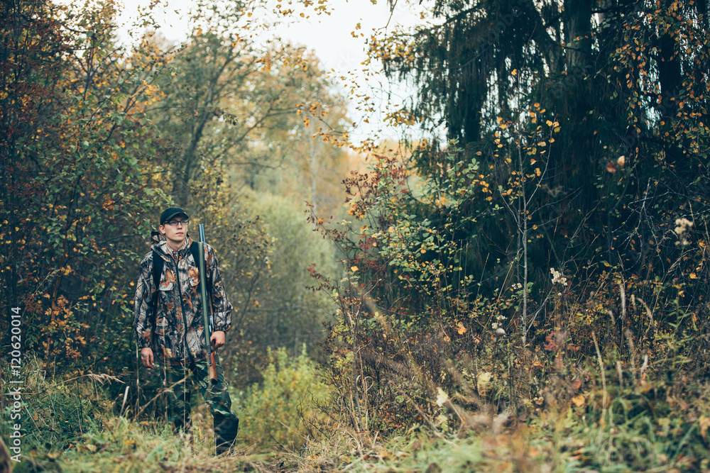 Male hunter in the autumn forest. A man holding a gun.