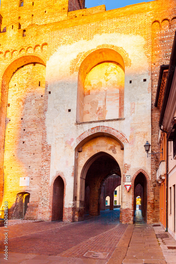 Defensive wall surrounding the small old town of Cittadella in Italy at sunrise. Entrance gate in the wall of red brick illuminated by sun.