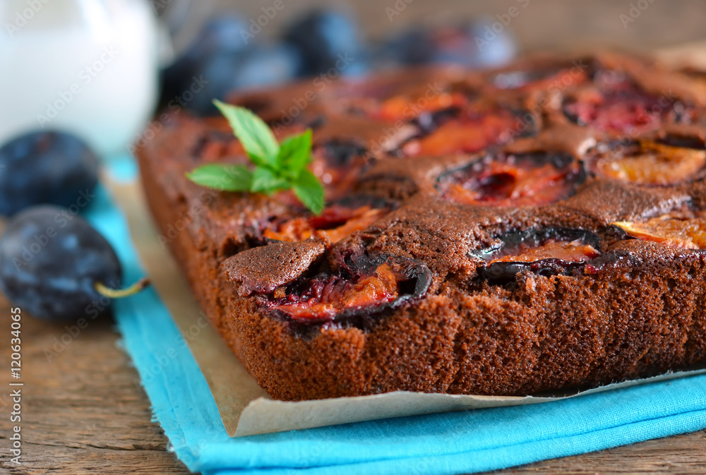 Chocolate cake with plums on a dark background with milk 