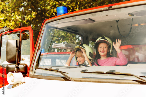  Two cute kids playing in fire truck, pretending to be firefighters, open doors day at fire station. Future profession for children. Educational programme for schoolkids