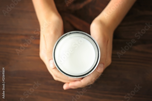 Female hands holding glass of fresh milk on wooden background