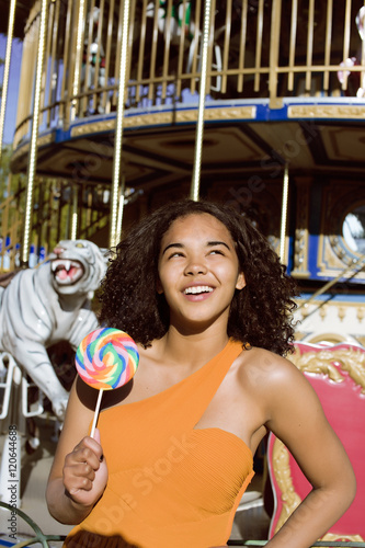 cool real teenage girl with candy near carousels at amusement park walking, having fun photo