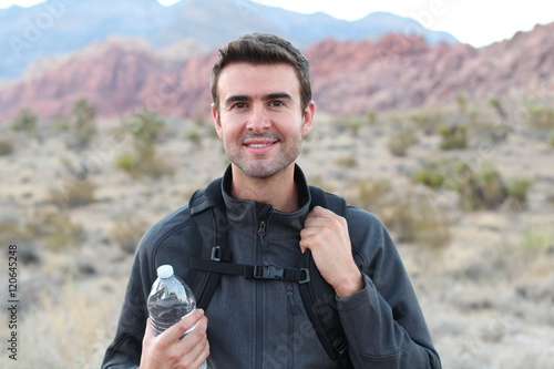 Adventure, travel, tourism, hike and people concept - man holding water bottle and black backpack hiking in the desert rocky mountains  photo