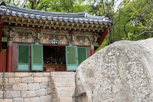 Ornate building behind a rock with engravings at the Beomeosa Temple in Busan, South Korea. Focused on the rock.