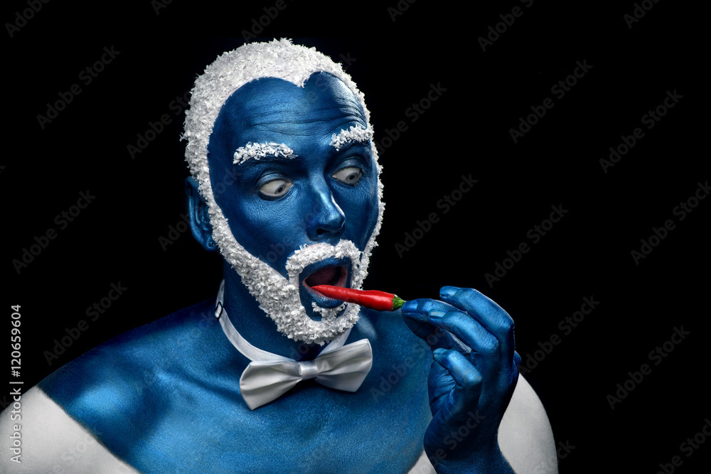 Man painted in blue color with snowy hair and beard eating chili pepper on black background Man painted in blue color with snowy hair and beard eating chili pepper on black background
