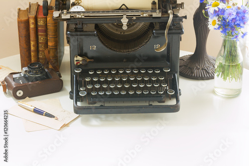 black vintage typewriter with books on white wooden table with copy space