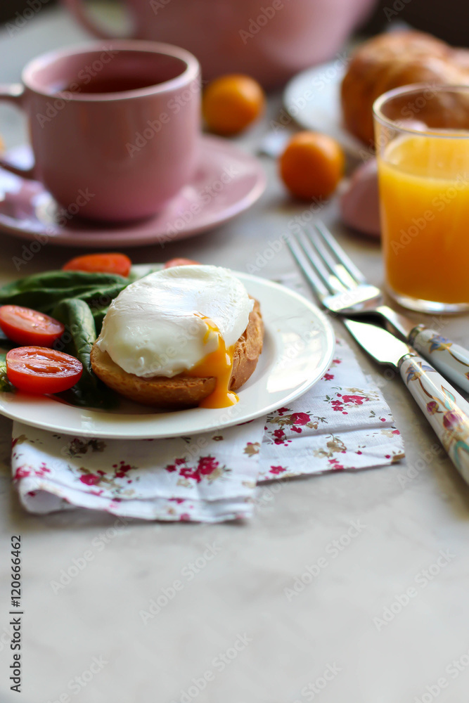 Breakfast with the poached egg on toast with spinach, tomatoes and orange juice, cup of tea coffee on kitchen the table