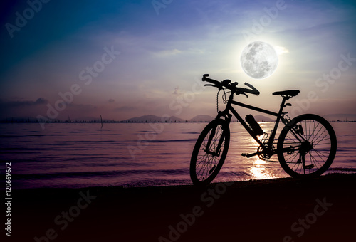 Silhouette of bicycle on the beach against beautiful full moon 