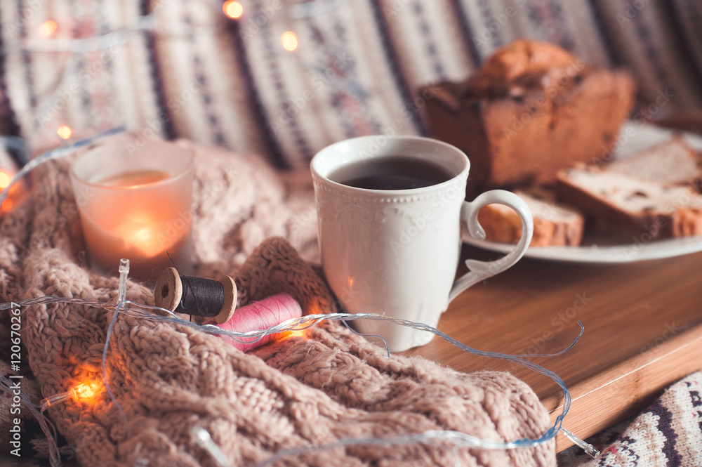 Cup of black tea with cake and candle staying on wooden tray in bed on knitted cloth closeup. Selective focus. Cup of black tea with cake and candle staying on wooden tray in bed on knitted cloth closeup. Selective focus.