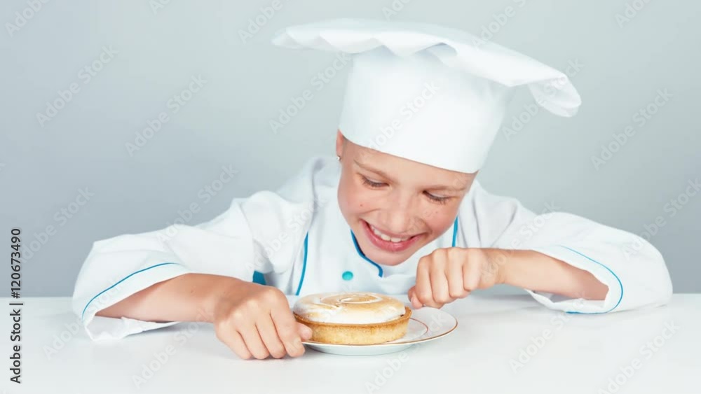 Close up portrait happy little chef cook looking at small cake with and smiling at camera Close up portrait happy little chef cook looking at small cake with and smiling at camera