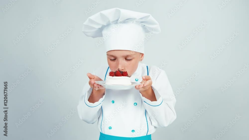 Close up portrait little chef baker holds meringue cake sniffing it and smiling at camera Close up portrait little chef baker holds meringue cake sniffing it and smiling at camera