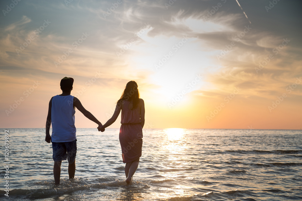 A young couple in love walks on the beach at sunset holding hands. The concept of love and affection, a date