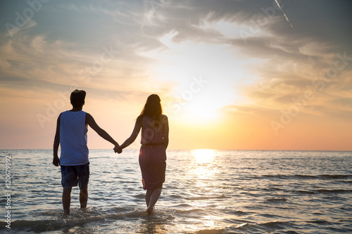 A young couple in love walks on the beach at sunset holding hands. The concept of love and affection  a date