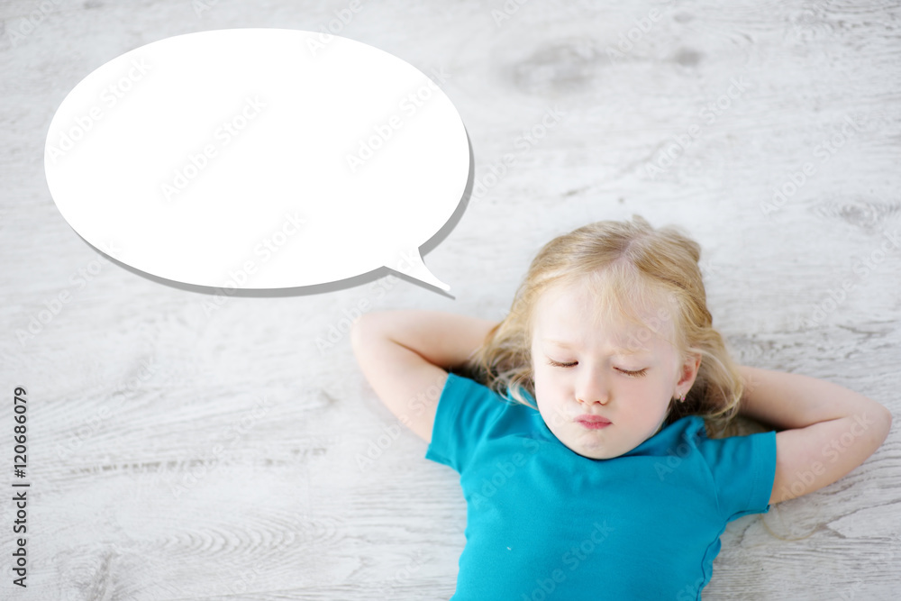 Fototapeta premium Little girl lying on white wooden floor with a speech bubble above her head