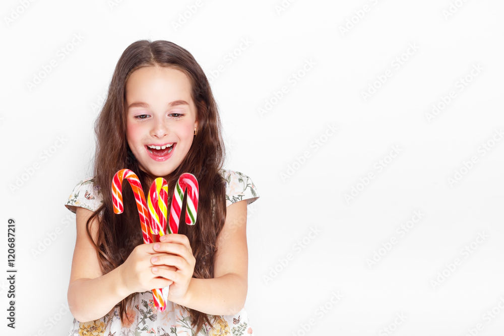 Happy, smiling cute little girl eating cristmas candy cane. Posing against a white wall. Happy, smiling cute little girl eating cristmas candy cane. Posing against a white wall.