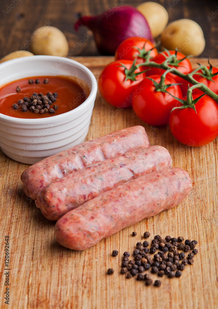 Raw beef sausages with tomatoes and sause on board Raw beef sausages with tomatoes and sause on board