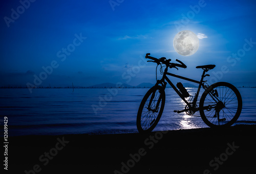 Silhouette of bicycle on the beach against bright full moon. Outdoors.