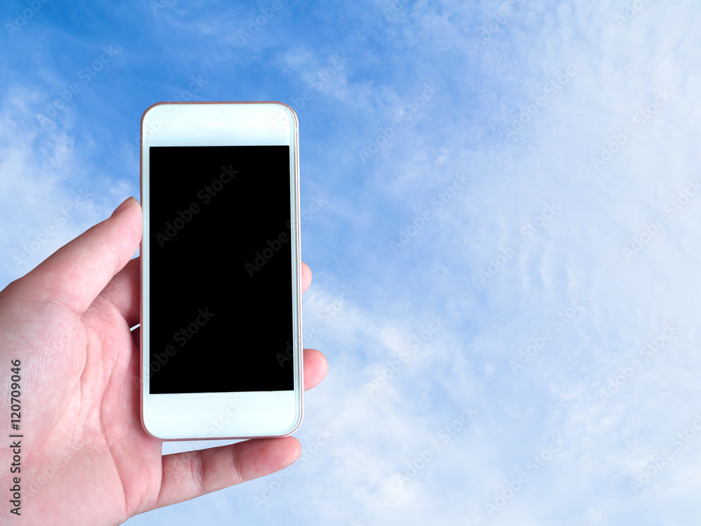 Left-hand holds the smartphone grey screen with sky background behind Left-hand holds the smartphone grey screen with sky background behind