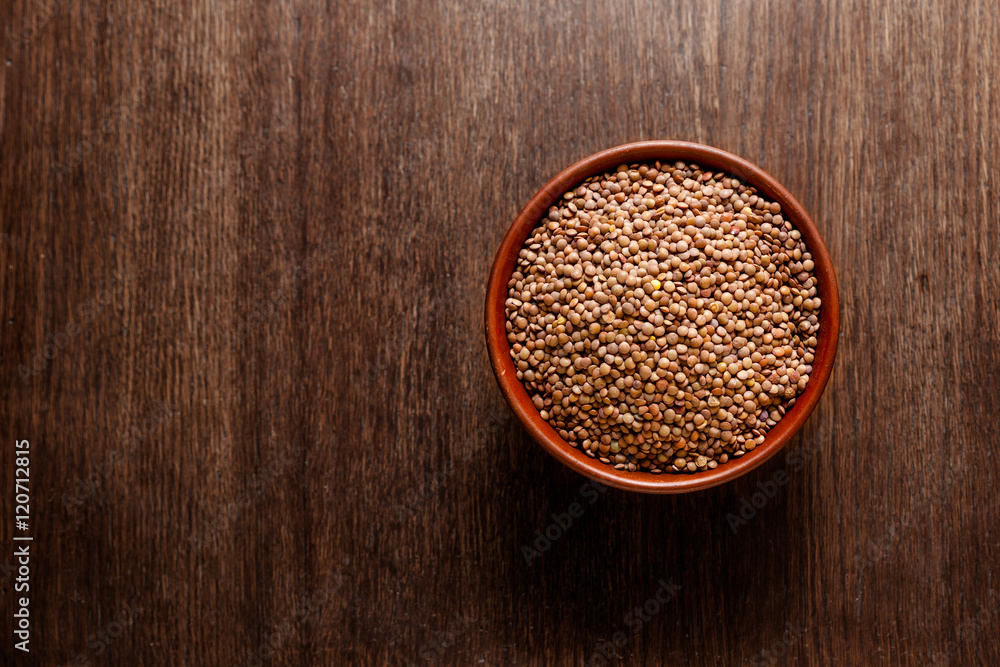 Rustic ceramic bowl of uncooked lentils isolated on dark wood from above Rustic ceramic bowl of uncooked lentils isolated on dark wood from above