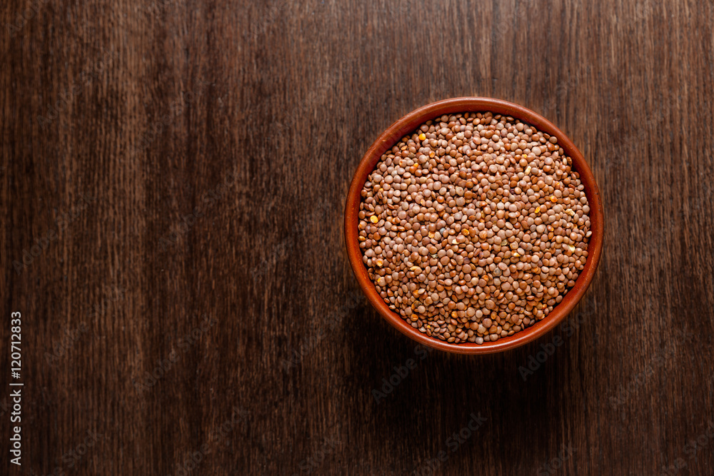 Rustic ceramic bowl of uncooked red lentils isolated on dark wood from above Rustic ceramic bowl of uncooked red lentils isolated on dark wood from above