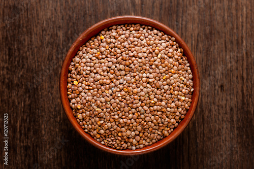 Rustic ceramic bowl of uncooked red lentils isolated on dark wood from above