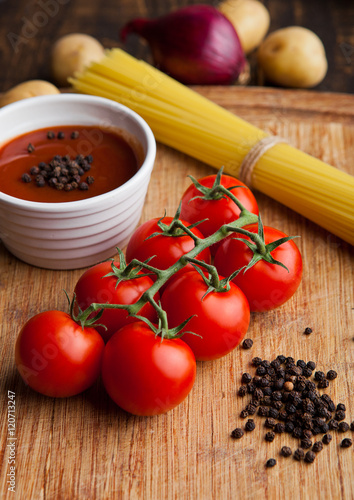 Fresh tomatoes with raw spagetti and pepper on kitchen board