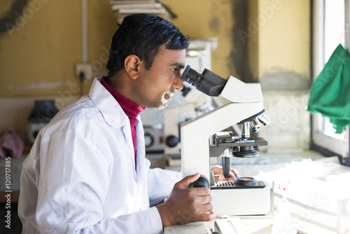 A lab technician working in a laboratory in a small hospital in Nepal looks into a microscope, Jiri, Solu Khumbu, Nepal photo