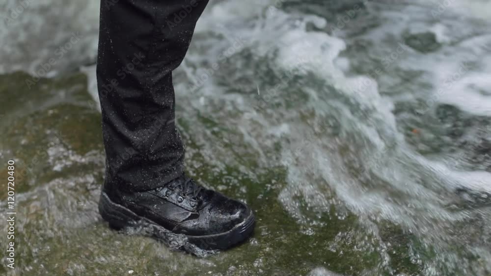 Detail of a male hiker’s boot as he stands at the bottom of a waterfall in slow motion. Detail of a male hiker’s boot as he stands at the bottom of a waterfall in slow motion.