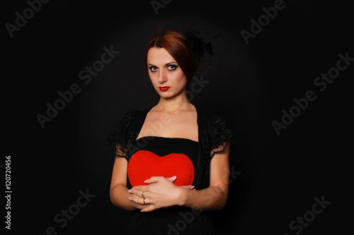 mysterious girl with a heart in his hands in a little black dress on a black background