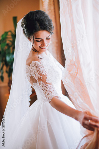 Portrait of beautiful bride with fashion veil posing on bed at window