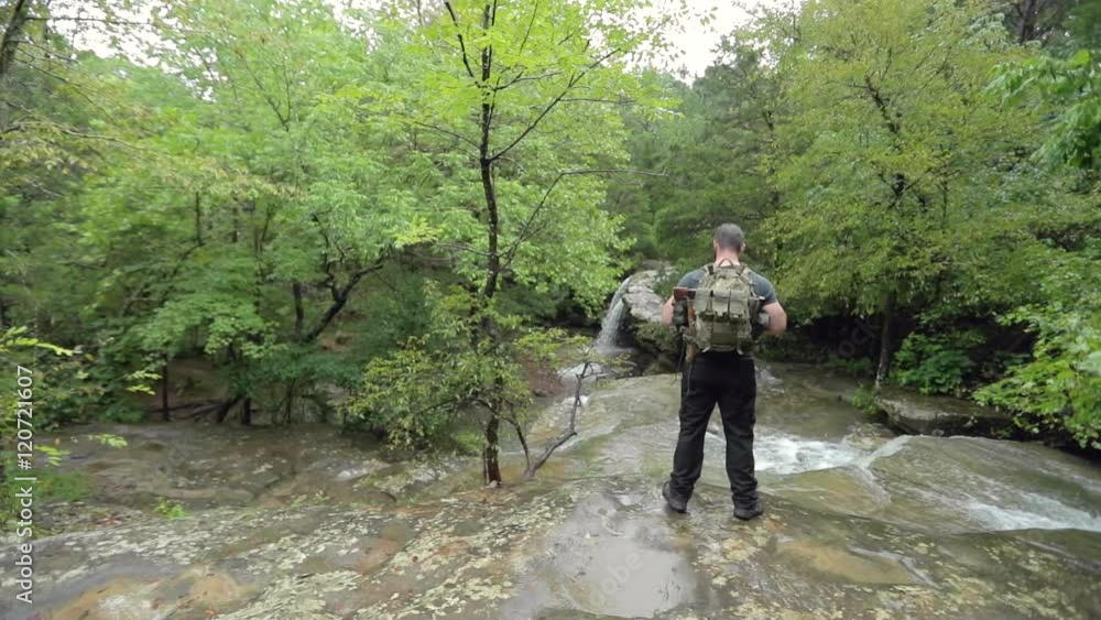 A male hiker stands at a creek at the top of a waterfall, in slow motion. A male hiker stands at a creek at the top of a waterfall, in slow motion.