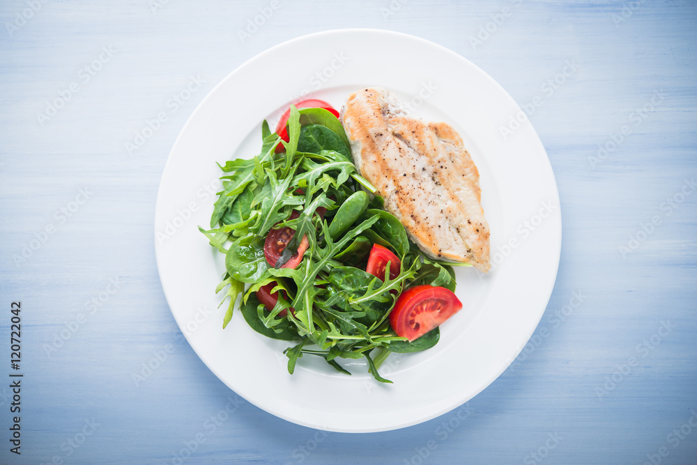 Roasted chicken breast and fresh salad with tomato and greens (spinach, arugula) top view on blue wooden background. Healthy food. Roasted chicken breast and fresh salad with tomato and greens (spinach, arugula) top view on blue wooden background. Healthy food.